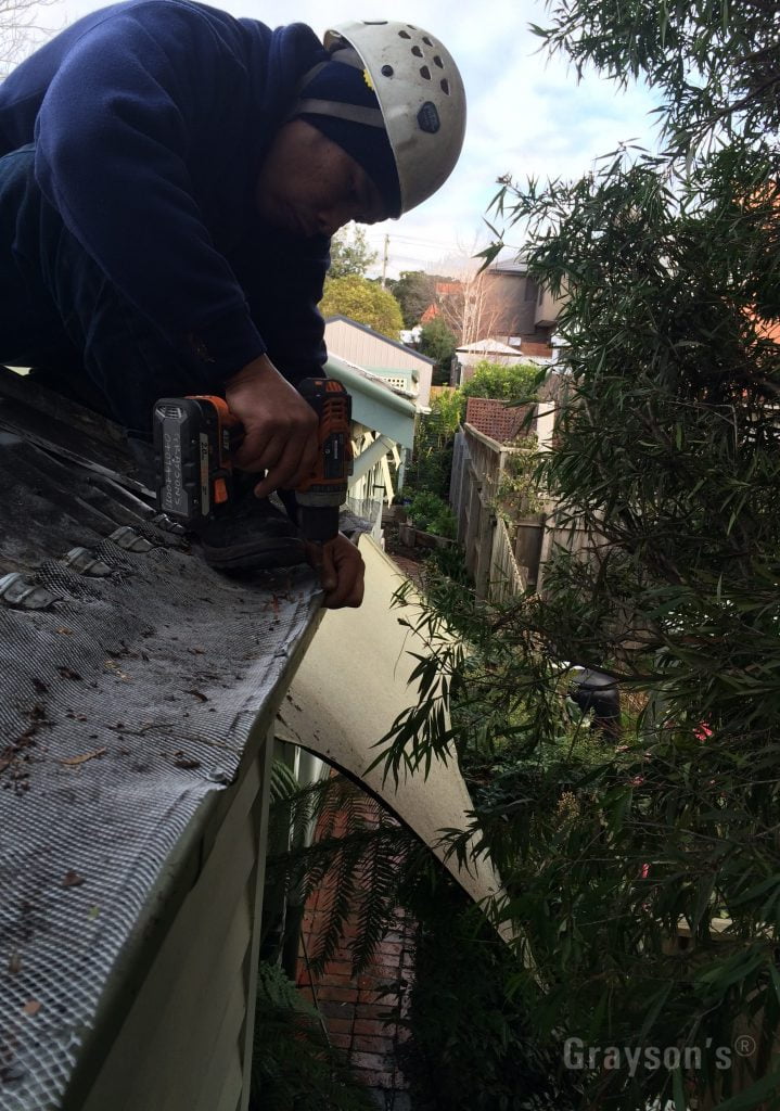 One of Grayson's Gutter Cleaning staff carefully repairing an old metal gutter cover.