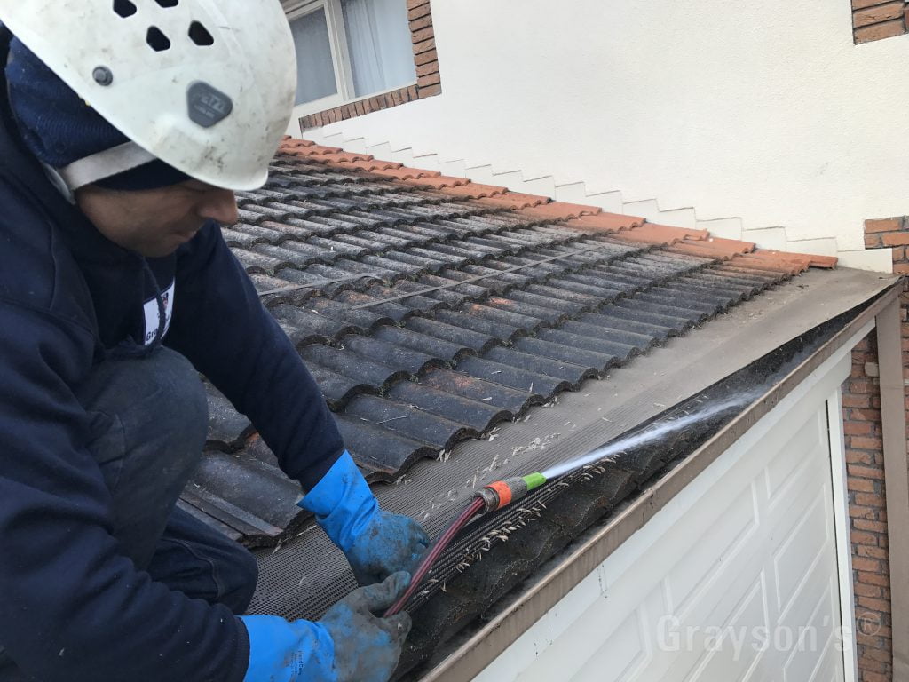 Lifting an old gutter mesh covering and flushing out the remaining sludge.
