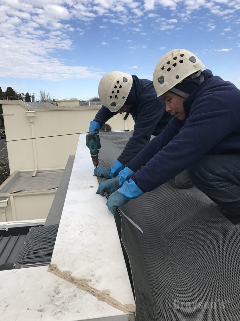 Attaching the gutter protection angle trim to the top of a parapet. This holds the ski-slope style system in place. Just to the left of the parapet is a piece of our gutter mesh covering a rain-head.