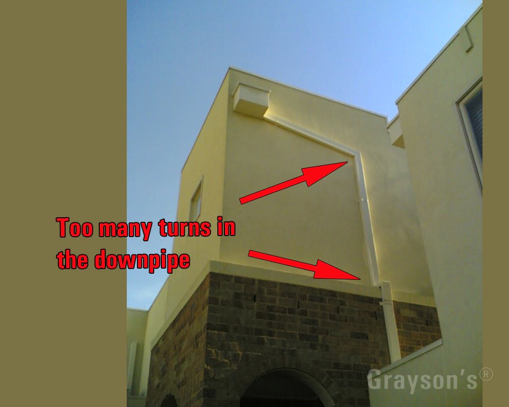 To accommodate the downpipe on this townhouse wall, the roof plumbers have had to install too many bends. The box at the top is called the 'rain-head.' Grayson's professional gutter cleaners will ensure your downpipe is flowing right!